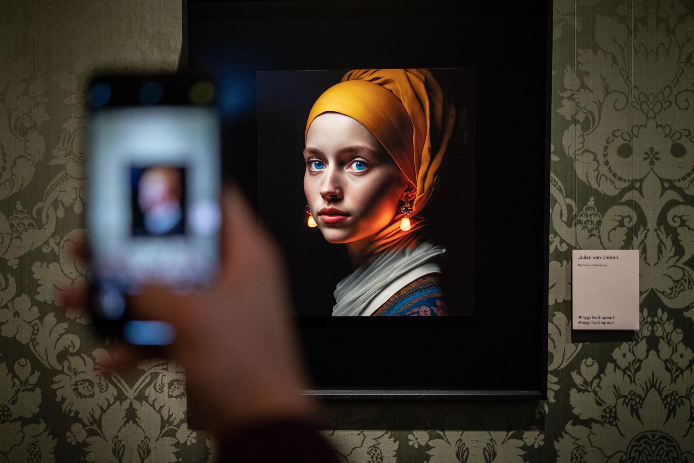 A visitor takes a picture with his mobile phone of an image designed with artificial intelligence by Berlin-based digital creator Julian van Dieken (C) inspired by Johannes Vermeers painting Girl with a Pearl Earring at the Mauritshuis museum in