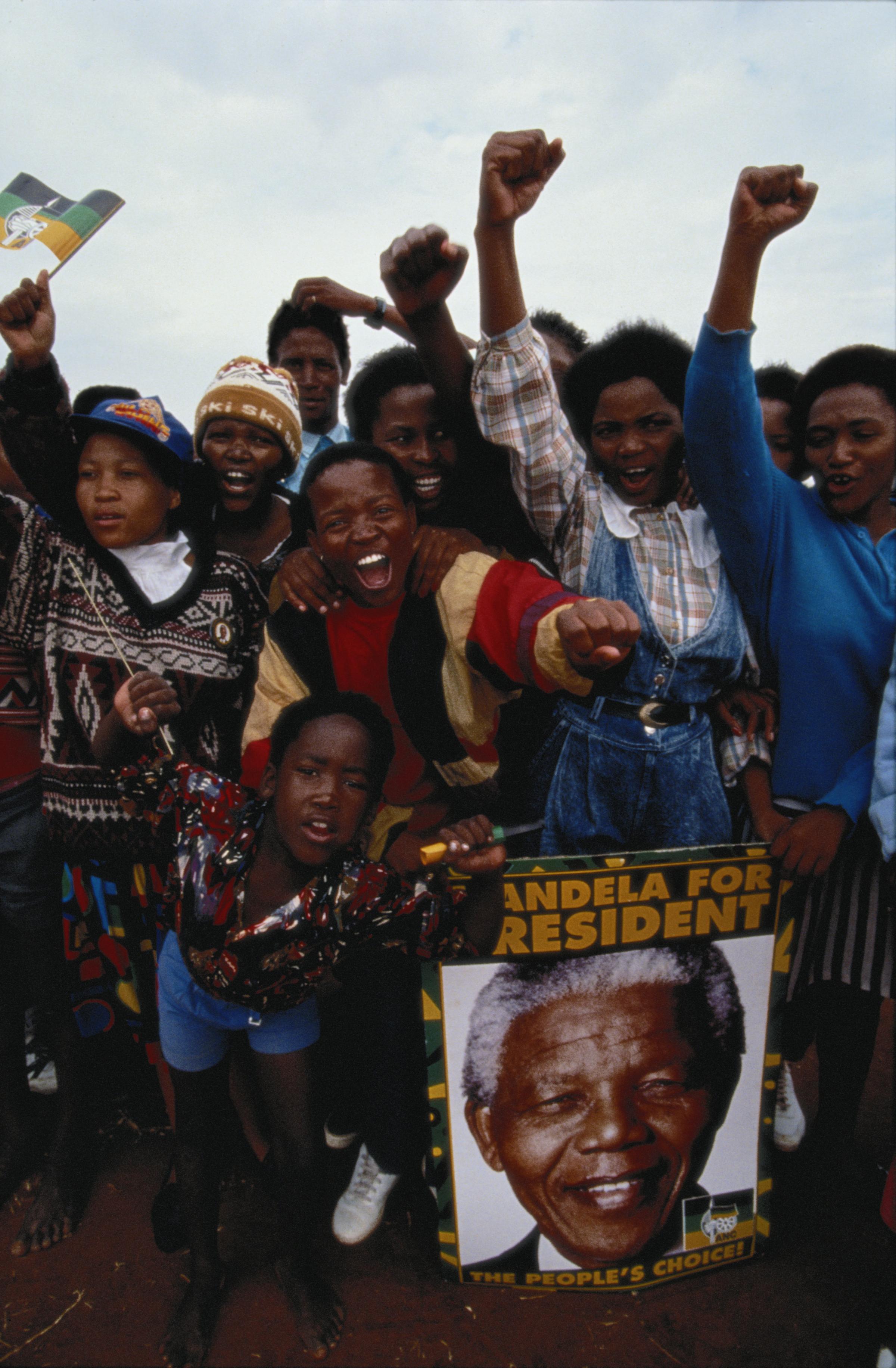Supporters of the African National Congress (ANC) give clenched fist salutes at a rally addressed by ANC leader Nelson Mandela in the run up to South Africas first General Election to be held with universal adult suffrage, April 1994. On the right is a